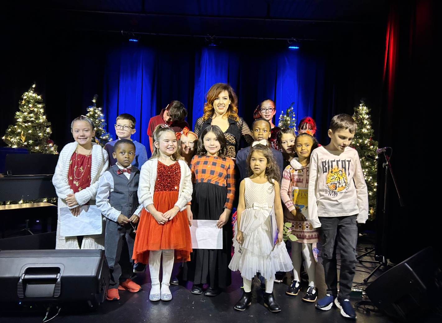 Miss Olivia with students at holiday recital with Christmas trees and stage lighting